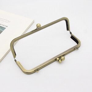 May include: A gold-toned metal frame for a purse or wallet with a decorative pattern and three round metal accents.