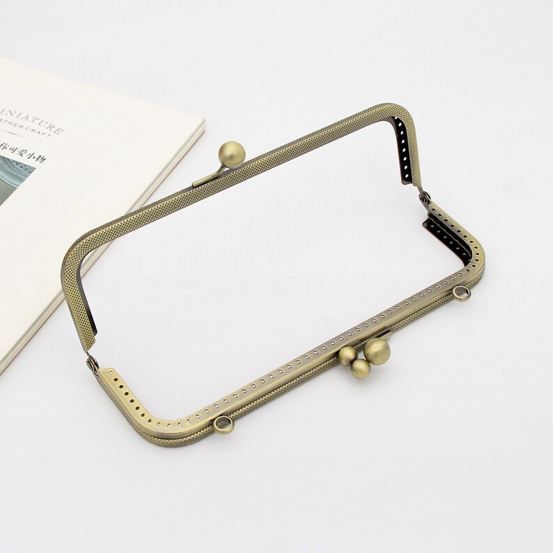 May include: A gold-toned metal frame for a purse or wallet with a decorative pattern and three round metal accents.