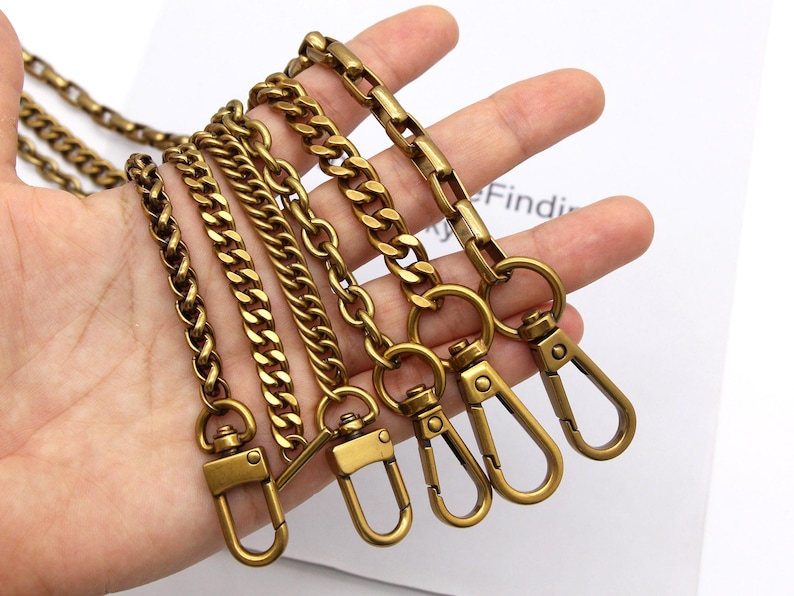 K&ouml;nnte beinhalten: Eine Auswahl an Kettenriemen in antikem Messingfarbton mit verschiedenen Gliederarten. Jede Kette hat einen passenden Verschluss zum Befestigen an einer Tasche oder einem anderen Gegenstand. Die Ketten werden vor wei&szlig;em Hintergrund gezeigt.