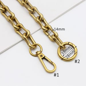 May include: Close-up of a gold-colored chain with a lobster clasp and a round ring clasp. The chain links are approximately 14mm wide. The ring clasp is 28mm in diameter and 19mm in inner diameter. The lobster clasp is labeled #1 and the ring clasp is labeled #2.