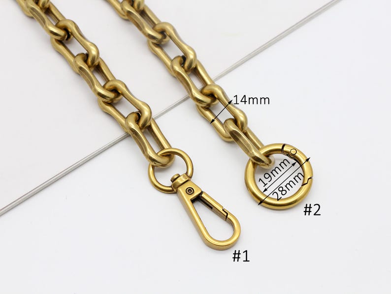 May include: Close-up of a gold-colored chain with a lobster clasp and a round ring clasp. The chain links are approximately 14mm wide. The ring clasp is 28mm in diameter and 19mm in inner diameter. The lobster clasp is labeled #1 and the ring clasp is labeled #2.