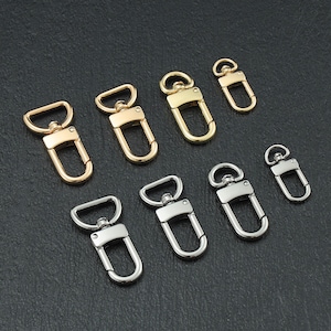 Puede incluir: Surtido de cierres giratorios dorados y plateados, también conocidos como broches de presión, en varios tamaños. Estos cierres metálicos se utilizan comúnmente para sujetar correas, correas o otros accesorios.