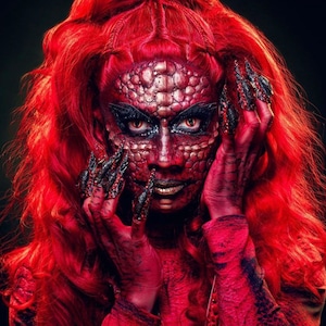 Könnte beinhalten: Eine Person mit roten Haaren und rotem Make-up, die einem Drachen ähnelt, mit langen, scharfen Krallen an den Fingern.