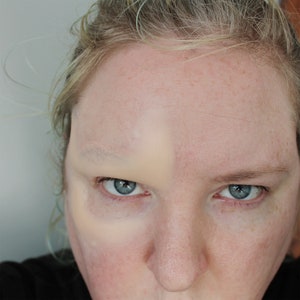 Pu&ograve; includere: Primo piano di un viso con un occhio coperto da trucco. Il trucco &egrave; di colore beige chiaro e copre l'intera palpebra e l'osso sopraccigliare. L'altro occhio &egrave; scoperto.