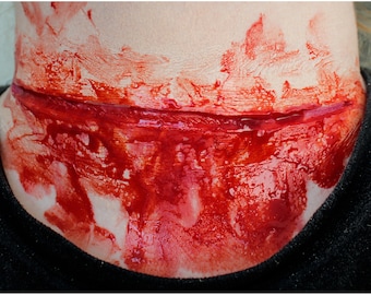 May include: A close-up of a fake, bloody wound on a person's neck. The wound is a deep cut with red and white paint, simulating blood.
