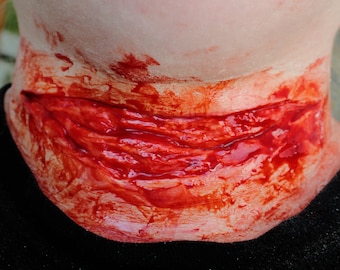 May include: A close-up of a fake, bloody wound on a person's neck. The wound is deep and appears to be fresh, with a lot of blood.