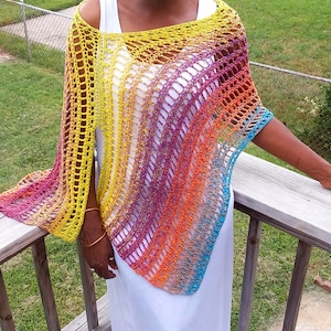 Könnte beinhalten: Ein Regenbogen-Häkelponcho mit einem zarten Muster. Der Poncho ist aus einem Farbverlaufsgarn gefertigt, das mit Gelb beginnt und in Orange, Rot, Lila und Blau übergeht.