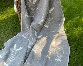 May include: A grey throw blanket with a white moose pattern. The blanket is folded and draped over a wicker chair.