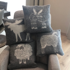 Peut inclure: Quatre coussins décoratifs avec différents motifs d'animaux. Les coussins sont gris avec des silhouettes d'animaux blanches. Les animaux sont un élan, un renne et deux moutons.