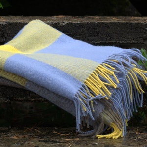 Op de afbeelding: Een blauwe en gele geruite deken met franjes. De deken is gevouwen en over een houten bank gelegd.