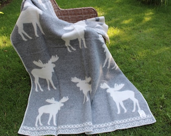 May include: A grey and white throw blanket with a pattern of white moose silhouettes. The blanket is folded and draped over a wicker chair.