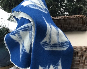 May include: A blue and white wool blanket with a sailboat pattern. The blanket is folded and draped over a wicker chair.