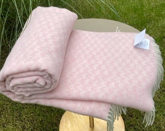 May include: A pink and white patterned throw blanket with a fringe border. The blanket is folded and displayed on a gold stand.