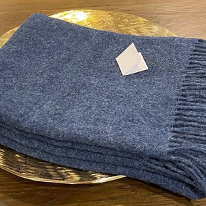 Op de afbeelding: Een blauwe deken met een franje rand. De deken is gevouwen en geplaatst op een gouden dienblad.