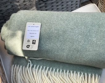 May include: A soft, green throw blanket with white fringe. The blanket is made of 100% New Zealand wool and measures 140x200 cm. The label also says "agave".