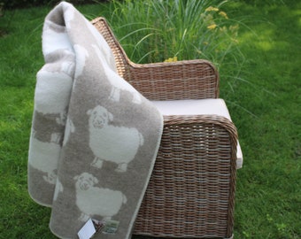 May include: A white and beige throw blanket with a sheep pattern draped over a wicker chair. The chair is sitting on a green lawn.