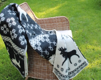 May include: A black and white patterned throw blanket with a reindeer design draped over a wicker chair. The blanket has a white border and is made of a soft, fuzzy material.