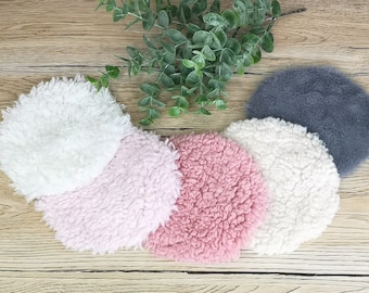 May include: Five round, fluffy, faux fur pads in various colours: white, pink, light pink, and grey. The pads are arranged in a semi-circle on a wooden surface.