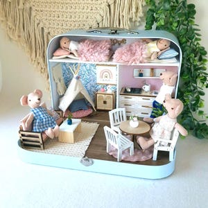 May include: A miniature dollhouse in a light blue suitcase, featuring two levels with bedrooms, a kitchen, and a living area. The dollhouse is furnished with tiny furniture, including beds, chairs, and a table, and populated with small bear dolls.