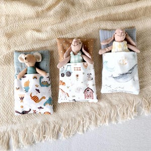 May include: Three stuffed animal toys, a mouse, a bunny, and a rabbit, are lying in their individual sleeping bags. Each sleeping bag has a different pattern. The mouse's sleeping bag has a dinosaur pattern, the bunny's sleeping bag has a farm animal pattern, and the rabbit's sleeping bag has a whale pattern.