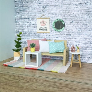 May include: A miniature living room set featuring a white sofa, a small white side table, a green plant in a pot, a pink cushion, a green and white cushion, a round mirror with a green wreath, a small white side table with a plant, a small birdcage, and a rug with pink, yellow and blue stripes.