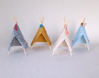 May include: Four miniature teepees made of felt in grey, yellow, white, and blue. Each teepee has a wooden stick frame and a decorative tassel.