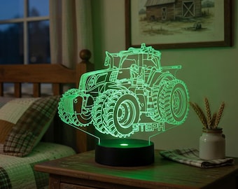 May include: A green tractor-shaped LED night light with the name "STEPH" etched into the base. The light sits on a black base and is placed on a wooden nightstand. A painting of a barn hangs on the wall in the background.