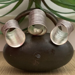 May include: Three silver rings with a textured, hammered finish. The rings are stacked on a dark gray stone.