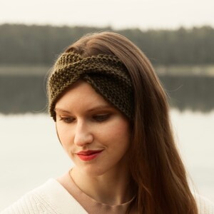 Pode incluir: Uma mulher usando uma faixa de cabeça de malha verde com um design trançado. A faixa é usada sobre a testa e cobre as orelhas. Ela está vestindo um suéter branco e tem cabelos longos e castanhos.