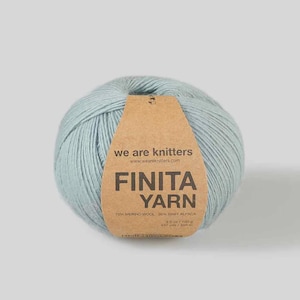 Op de afbeelding: Een bol lichtblauw Finita Yarn. Het etiket toont "we are knitters" en vermeldt de samenstelling: 70% merinowol en 30% baby alpaca. Het gewicht is 100g. De tekst "FINITA YARN" is ook zichtbaar.