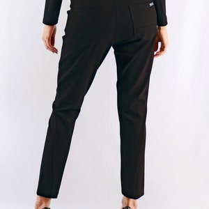 May include: Black trousers with a tailored fit, featuring back pockets and a small logo detail. The trousers are paired with black high-heeled shoes with red accents.