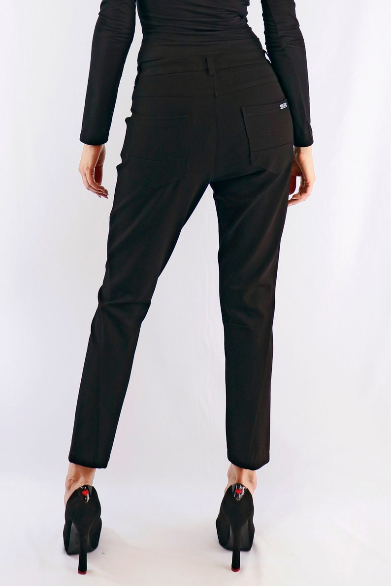 May include: Black trousers with a tailored fit, featuring back pockets and a small logo detail. The trousers are paired with black high-heeled shoes with red accents.