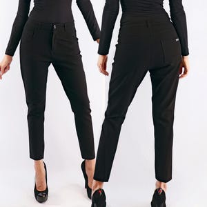 May include: Black pants with a button closure and pockets. The pants are shown from the front and back. The pants are a solid black color and appear to be made of a smooth fabric. The pants are worn with black heels.