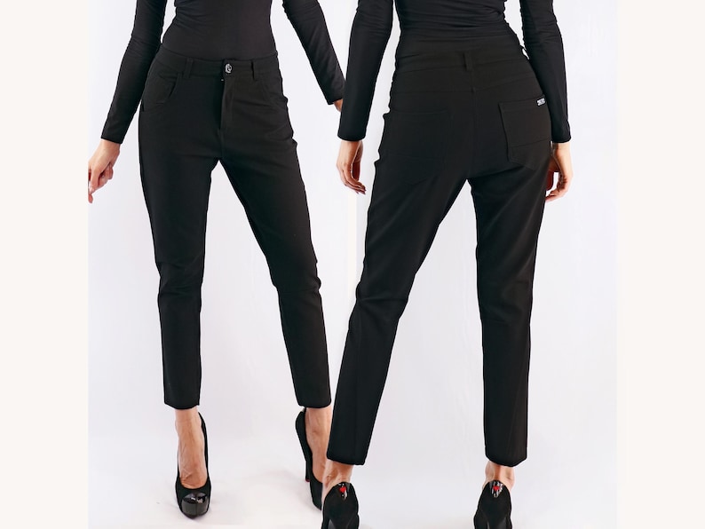 May include: Black pants with a button closure and pockets. The pants are shown from the front and back. The pants are a solid black color and appear to be made of a smooth fabric. The pants are worn with black heels.