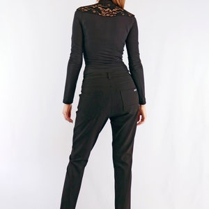 May include: Black long-sleeve top with a lace detail at the shoulders and a pair of black trousers. The outfit is completed with black high heels. The clothing is form-fitting and appears to be made of a smooth fabric.