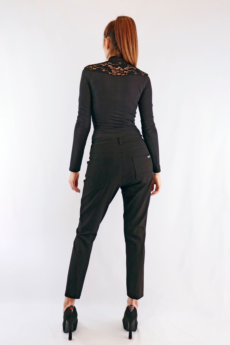 May include: Black long-sleeve top with a lace detail at the shoulders and a pair of black trousers. The outfit is completed with black high heels. The clothing is form-fitting and appears to be made of a smooth fabric.