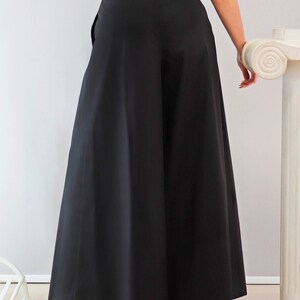 May include: Black wide-leg pants with a high waist. The pants have a full, flowing silhouette. The model is wearing a patterned top. The pants are a solid black color and appear to be made of a lightweight fabric.