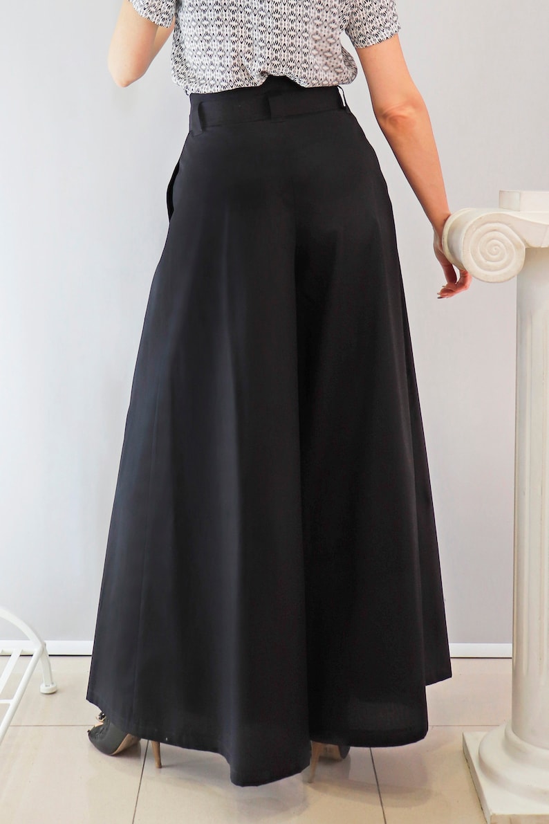 May include: Black wide-leg pants with a high waist. The pants have a full, flowing silhouette. The model is wearing a patterned top. The pants are a solid black color and appear to be made of a lightweight fabric.