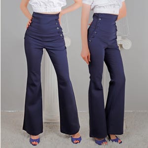 May include: Navy blue high-waisted pants with a flared leg. The pants feature a row of buttons on each side of the waist. The model is wearing blue open-toe heels. The pants are a classic style.