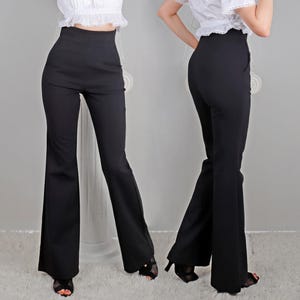 May include: Black high-waisted flared pants. The pants have a fitted waist and a wide, flowing leg. The fabric appears to be a smooth, solid color. The pants are shown on a model.