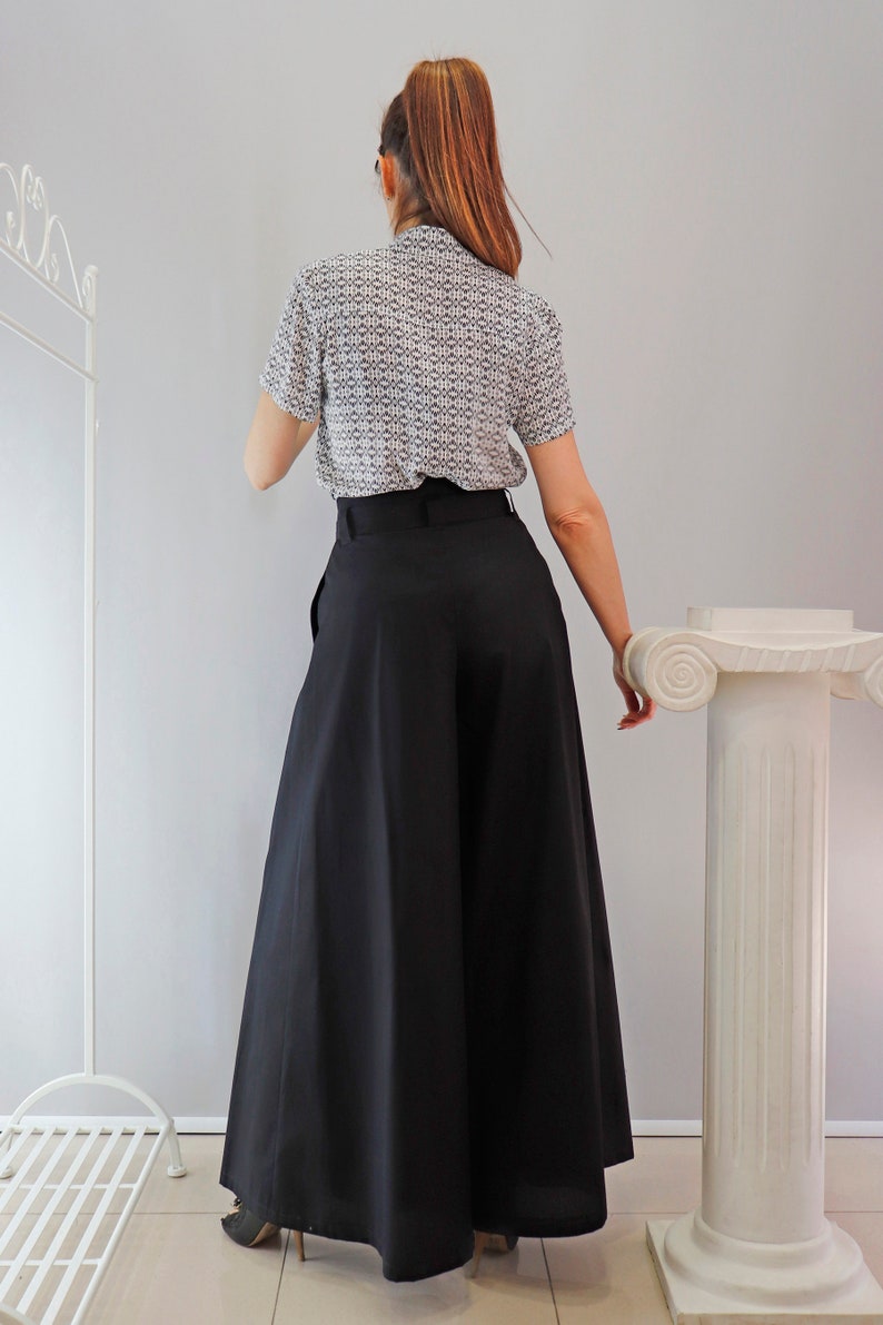 May include: A woman wearing a short-sleeved blouse with a small geometric pattern in black and white, paired with wide-leg black pants. The pants have a high waist and a flowing silhouette. The outfit is simple and elegant.