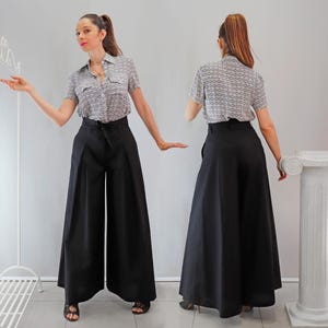 May include: A woman wearing a short-sleeved, patterned button-up shirt and high-waisted, wide-leg black pants. The pants have a tie at the waist. The outfit is suitable for a variety of occasions.