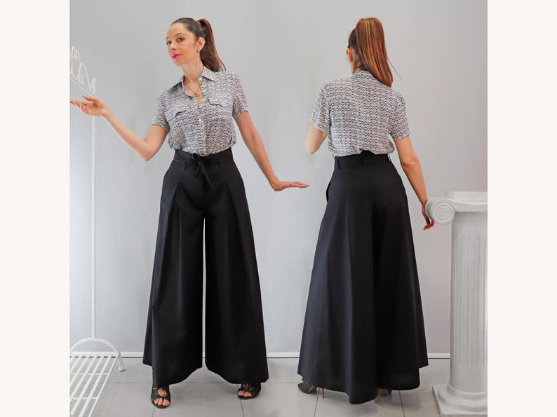 May include: A woman wearing a short-sleeved, patterned button-up shirt and high-waisted, wide-leg black pants. The pants have a tie at the waist. The outfit is suitable for a variety of occasions.