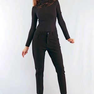 May include: A black long-sleeved top with a lace neckline paired with black trousers. The outfit is completed with black high-heeled shoes. The clothing is form-fitting and suitable for a variety of occasions.