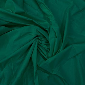 May include: A solid dark emerald green fabric with a smooth, matte texture. The material is gathered and draped in the center, creating deep, soft folds and shadows that highlight the rich, consistent color throughout the entire surface.