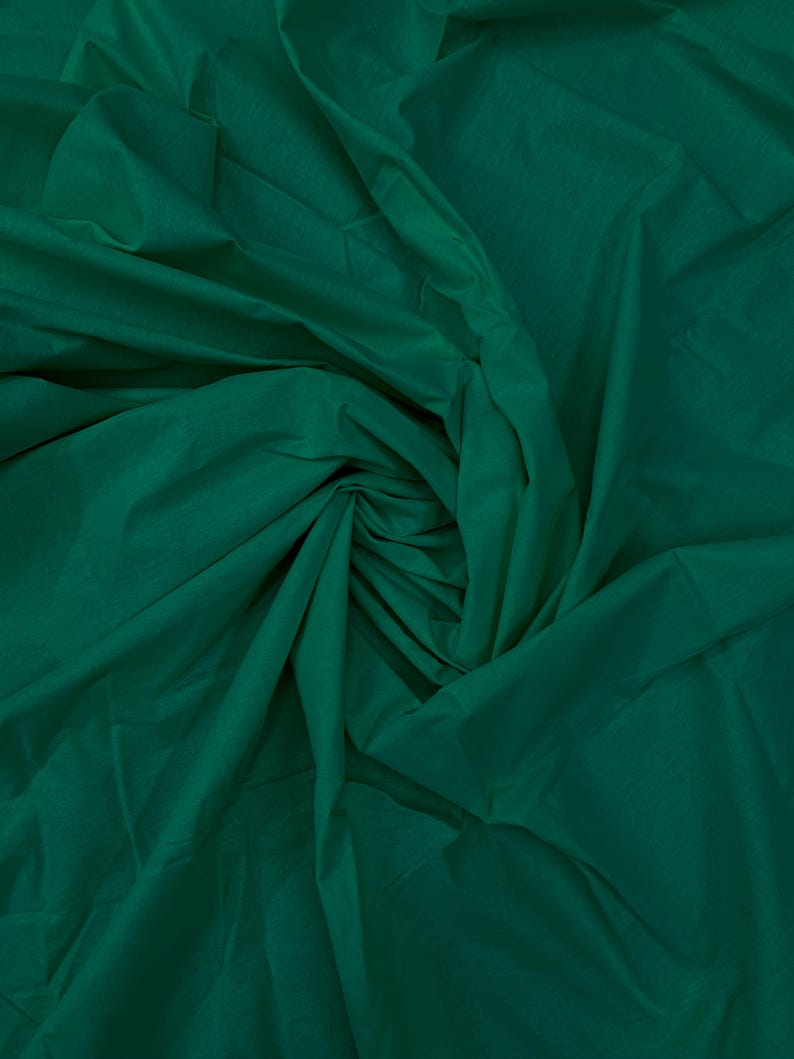 May include: A solid dark emerald green fabric with a smooth, matte texture. The material is gathered and draped in the center, creating deep, soft folds and shadows that highlight the rich, consistent color throughout the entire surface.