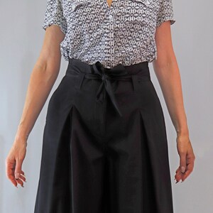 May include: A short-sleeved button-down shirt with a black and white pattern is paired with high-waisted, wide-leg black pants. The pants feature a tie-waist detail. The outfit is a stylish ensemble, suitable for various occasions.