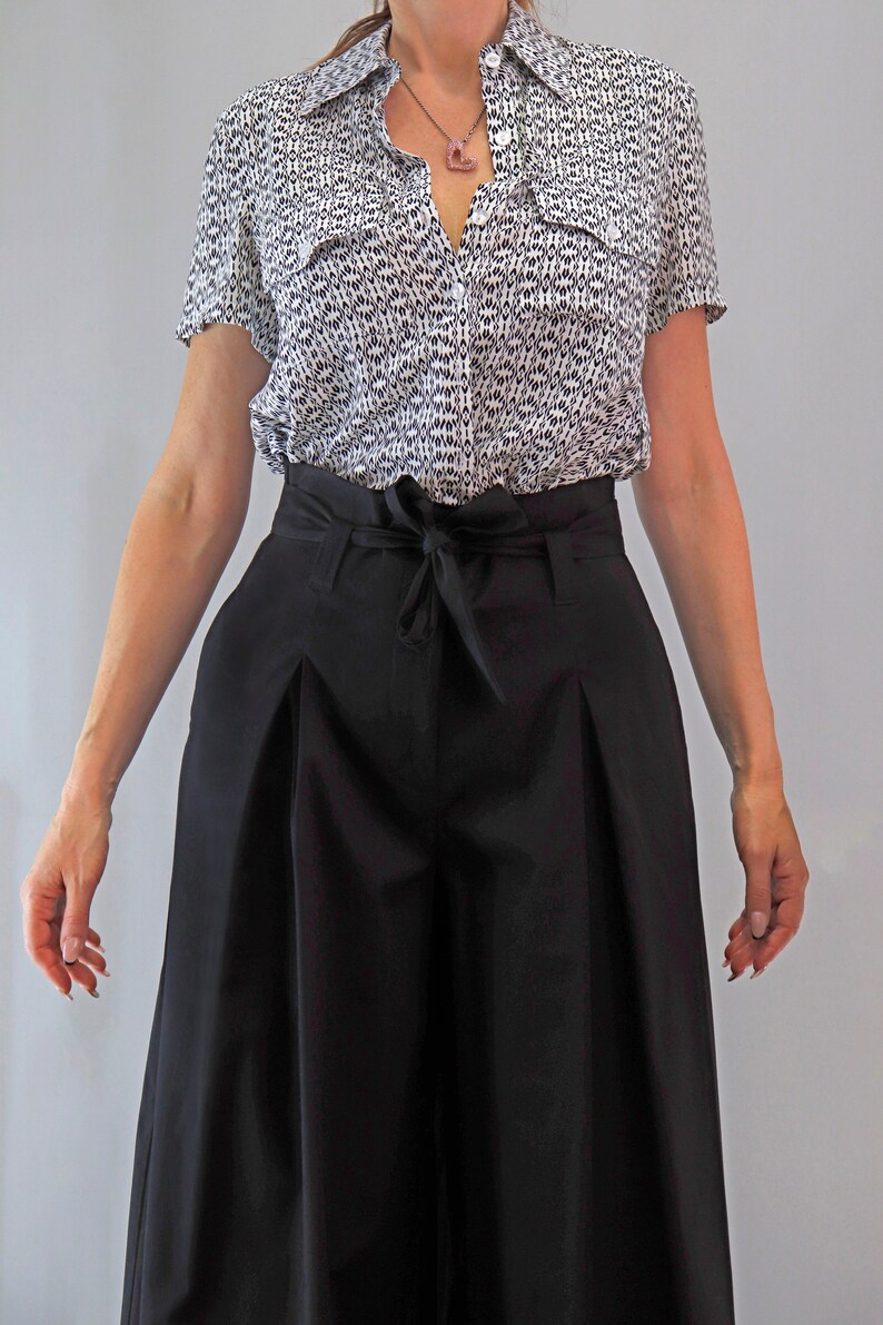 May include: A short-sleeved button-down shirt with a black and white pattern is paired with high-waisted, wide-leg black pants. The pants feature a tie-waist detail. The outfit is a stylish ensemble, suitable for various occasions.