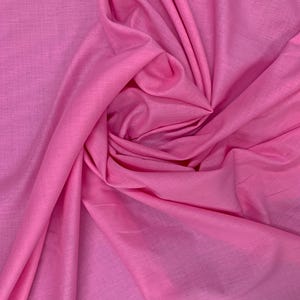 May include: A solid bright pink fabric with a visible woven texture. The material is draped in a central swirl, creating soft folds and shadows that highlight the consistent color and the fine, interlaced pattern of the textile fibers throughout.