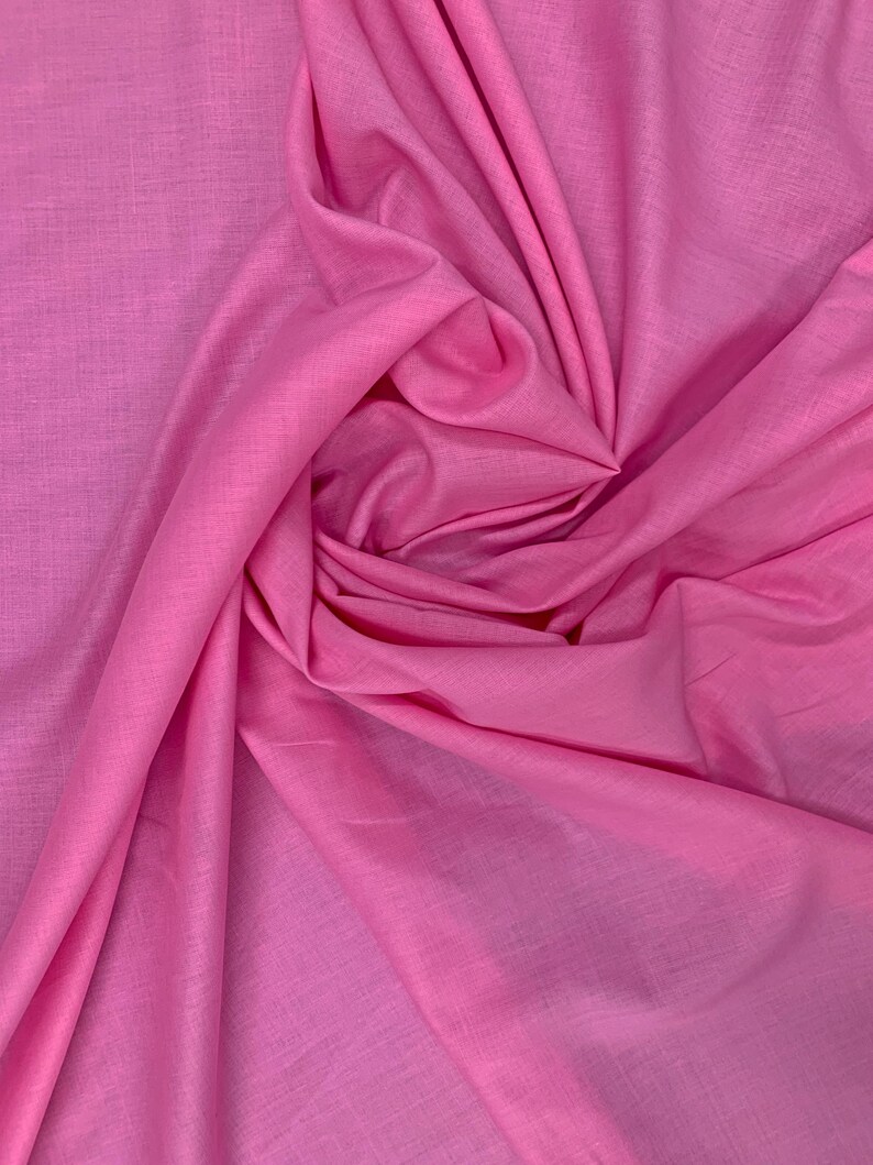 May include: A solid bright pink fabric with a visible woven texture. The material is draped in a central swirl, creating soft folds and shadows that highlight the consistent color and the fine, interlaced pattern of the textile fibers throughout.